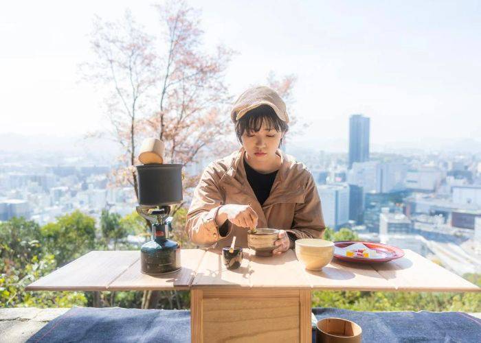 Atop Mt. Futaba, a Japanese tea ceremony is taking place in front of the Hiroshima City skyline.